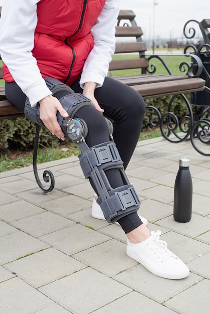 Vrouw die een kniebrace of orthese draagt na een beenoperatie die in het park loopt