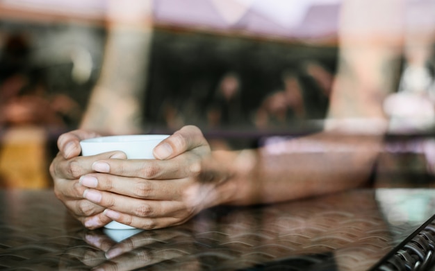 Foto vrouw die een kop van hete koffie in koffie houdt dichtbij venster