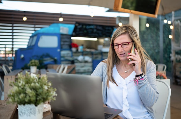 Vrouw die een laptop gebruikt en de mobiele telefoon beantwoordt