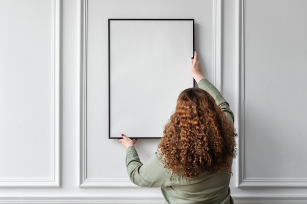 Foto vrouw die een leeg fotolijstje aan de muur hangt