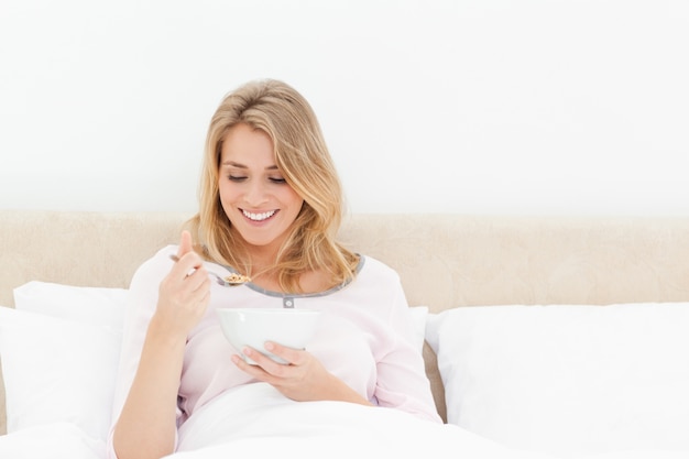 Vrouw die een lepel graangewas bekijkt terwijl het zitten in bed