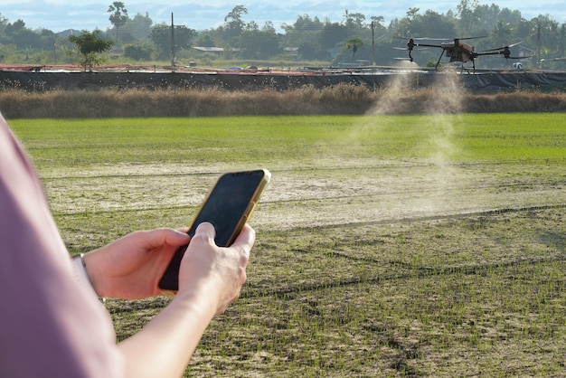 Vrouw die een mobiele telefoon gebruikt op een boerderij omringd door landbouwcontrole Petrol Drone Sprayer