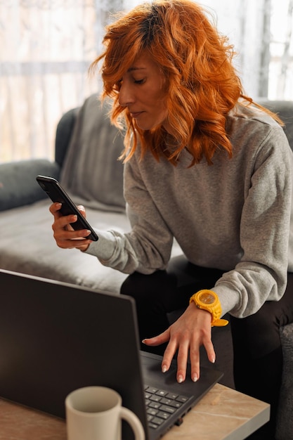 Vrouw die een smartphone en een laptop thuis gebruikt