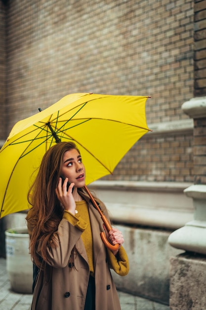 Vrouw die een smartphone gebruikt en een gele paraplu vasthoudt