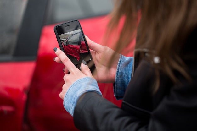 Vrouw die een smartphone gebruikt om een foto te maken van de schade aan haar auto veroorzaakt door een auto-ongeluk