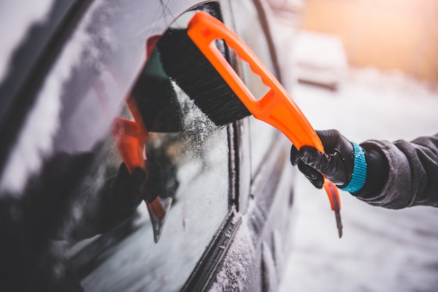 Vrouw die een sneeuw behandelde auto schoonmaakt