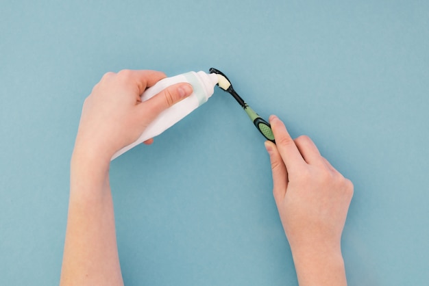 Vrouw die een tandpasta op haar tandenborstel met handen op blauw drukt