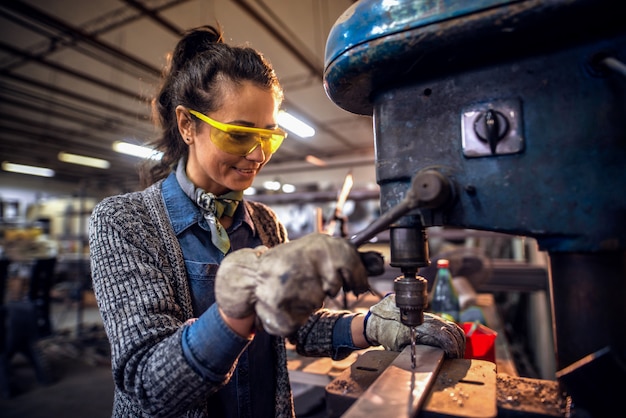 Vrouw die een verticale machine met behulp van om een gat in metaal te maken terwijl status in workshop