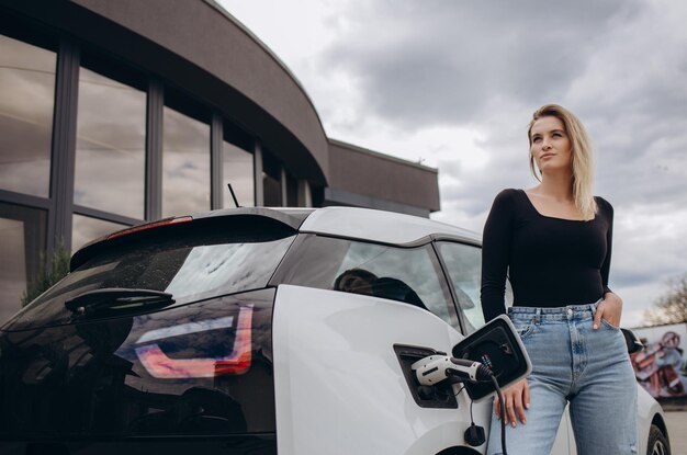 Vrouw die elektroauto laden door haar huis en lader houden