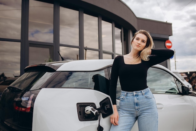 Vrouw die elektrocar laadt bij het elektrische benzinestation