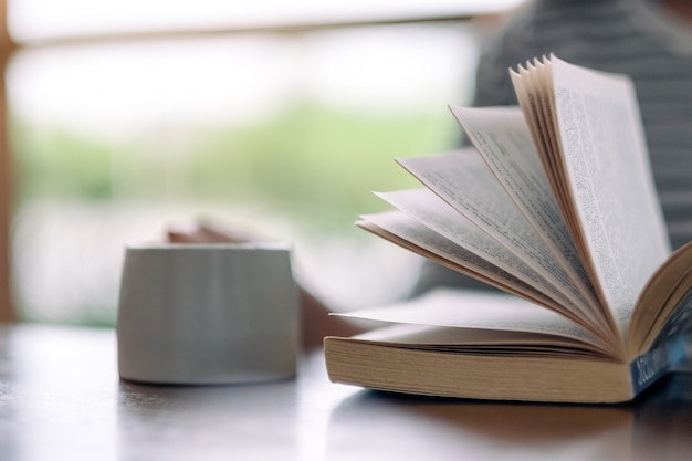 vrouw die en een boek houdt leest terwijl het drinken van koffie op houten lijst