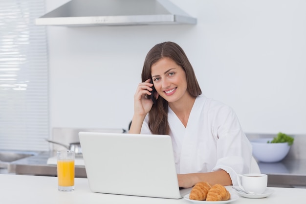 Vrouw die en laptop telefoneert gebruikt