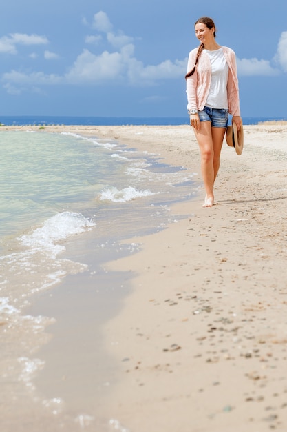 Vrouw die en op het strand tegen het overzees glimlacht loopt