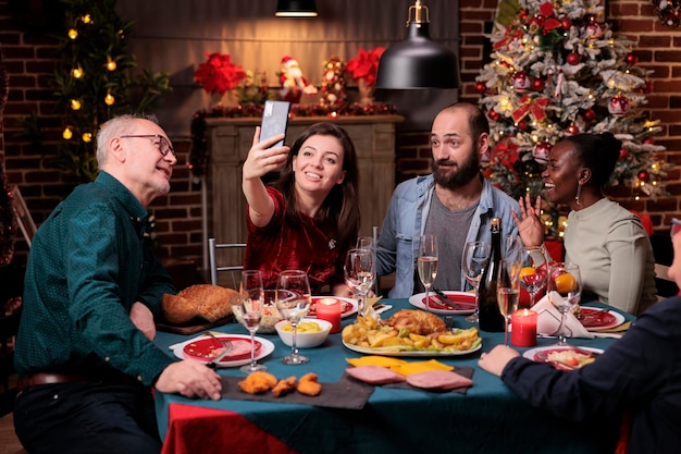 Vrouw die familieportret selfie neemt op smartphone, samen kerst vieren aan feestelijke eettafel. Kerstvakantie vieren, mensen verzamelen, traditionele maaltijd eten