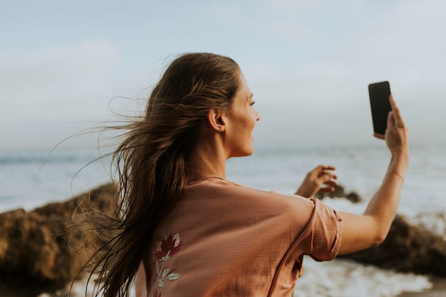 Vrouw die foto&#39;s met haar telefoon op het strand neemt