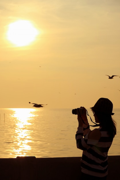 vrouw die foto van vliegende meeuwen tijdens de zonsopgang boven de Golf van Thailand