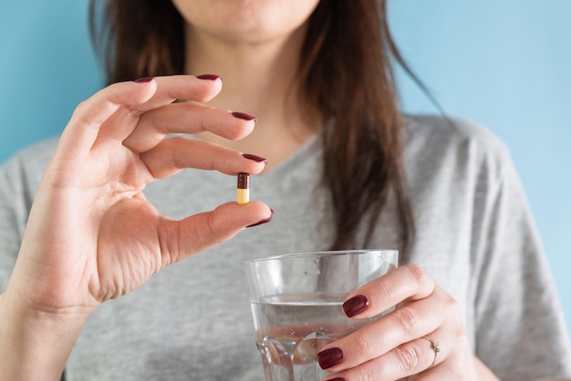 Vrouw die gastritis maagzweer zuurbranden geneeskunde capsule of pil op blauwe achtergrond met glas water