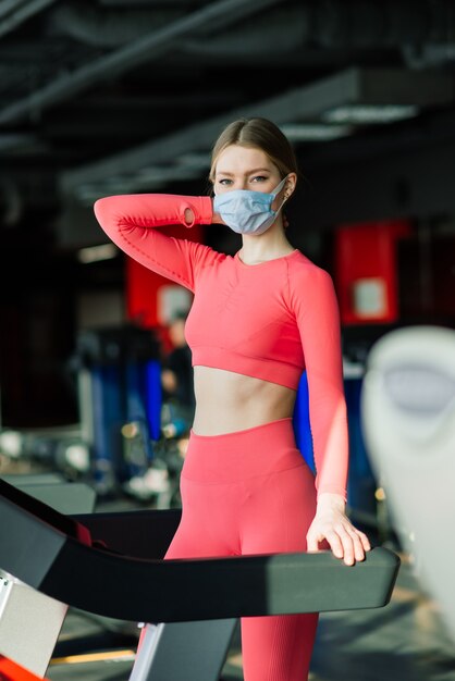 Vrouw die gezichtsmasker draagt, oefent training in de sportschool tijdens coronavirus pandermic, covid