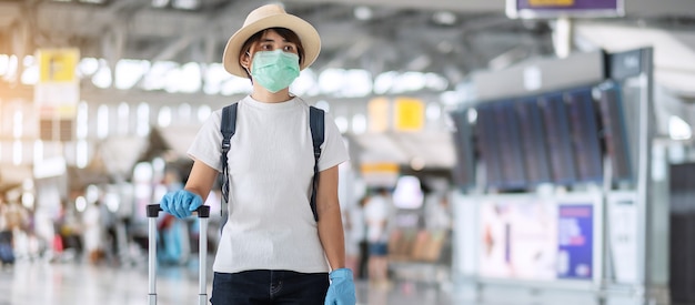 Vrouw die gezichtsmasker en nitrilhandschoen draagt ?? die handvatbagage in luchthaven houdt