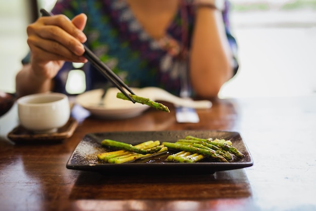 Vrouw die grillasperges met houten eetstokjes eet in restaurant