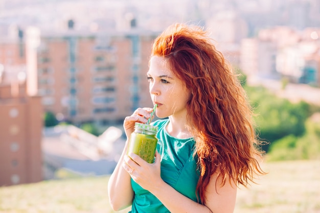 Vrouw die groen vitaminesap in openlucht drinkt