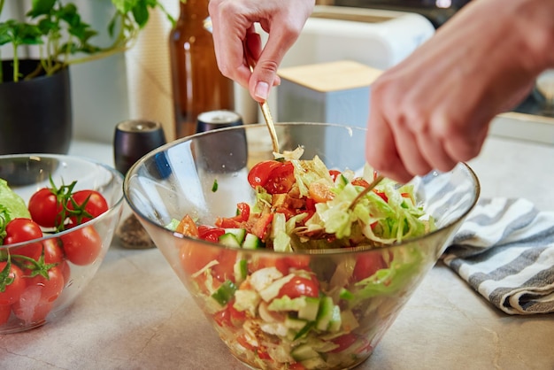 Vrouw die groene groentesalade in kom mengt bij keuken