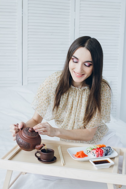 Vrouw die groene thee drinkt en sushi eet