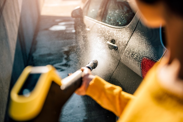 Vrouw die haar auto met hogedrukreiniger wast