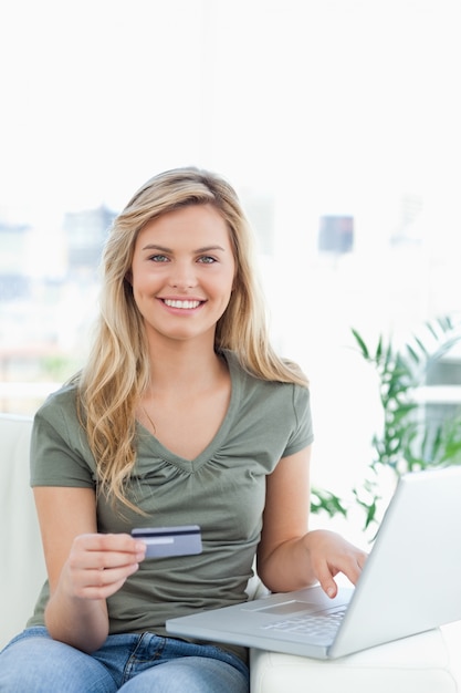 Vrouw die haar creditcard en laptop op de laag met behulp van terwijl het glimlachen