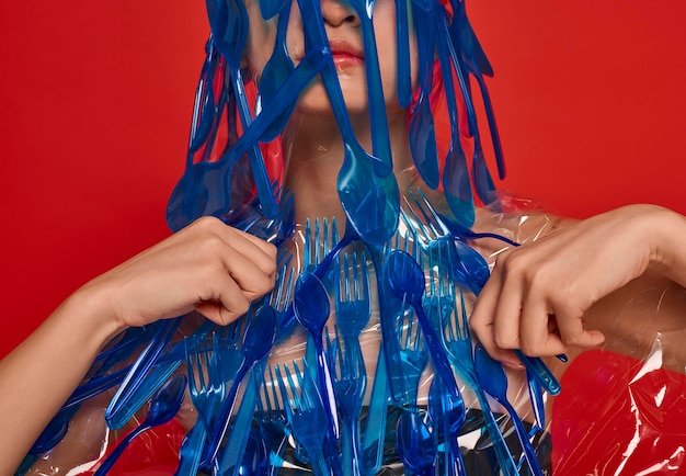 Vrouw die haar gezicht en lichaam bedekt met blauw plastic vaatwerk