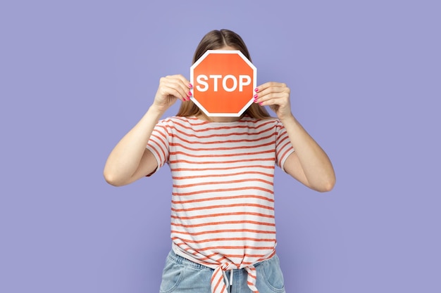 Vrouw die haar gezicht vasthoudt en verbergt met rood stopbord aandacht voor veilige oversteekplaats