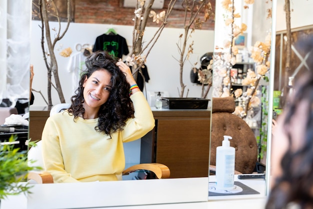 Vrouw die haar haar aanraakt terwijl ze voor een spiegel staat in een schoonheidssalon