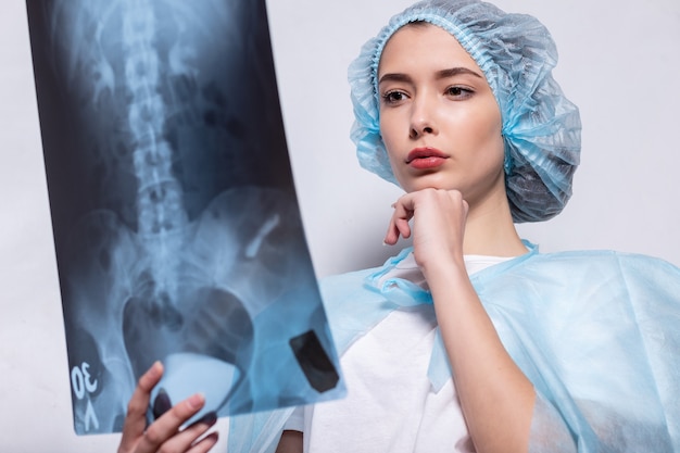 Vrouw die haar hand opsteekt en een röntgenfoto vasthoudt. Dokter onderzoekt röntgenfoto. Vrouw met beschermend masker met haar hand en houdt een momentopname van de longen vast.