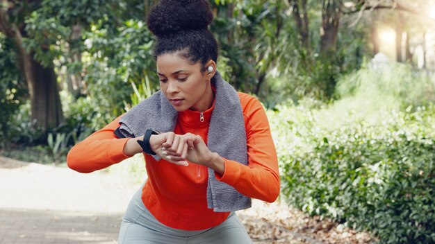 Vrouw die haar hartslag controleert met een smartwatch tijdens een gezondheids-, fitness- en wellnessloop in de natuur Actief meisje aan het joggen voor een cardio-oefening in een buitenpark met een activity tracker en handdoek