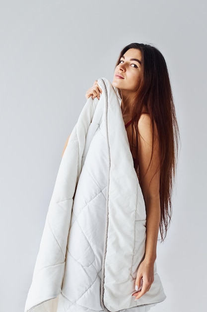 Vrouw die haar lichaam bedekt met een handdoek in de studio tegen een witte achtergrond.