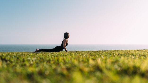 Vrouw die haar lichaam uitrekt liggend op het gras buiten in de middag. Kopieer ruimte