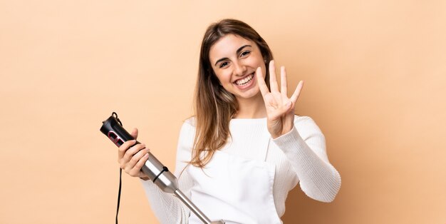 Vrouw die handmixer over geïsoleerde muur gelukkig gebruikt en vier met vingers telt