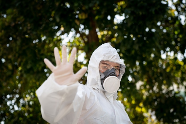 Vrouw die handschoenen met biohazard chemisch beschermend pak en masker draagt. Met ongelukkig gezicht. Vrouw houdt de hand voor haar, teken om te stoppen, stopbord.