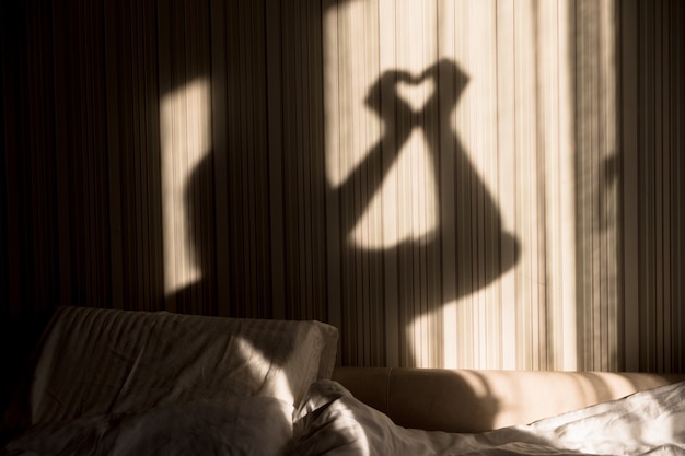 Vrouw die hartschaduw met haar handen op de muur maakt. Werelddag voor geestelijke gezondheid, hoop en liefde