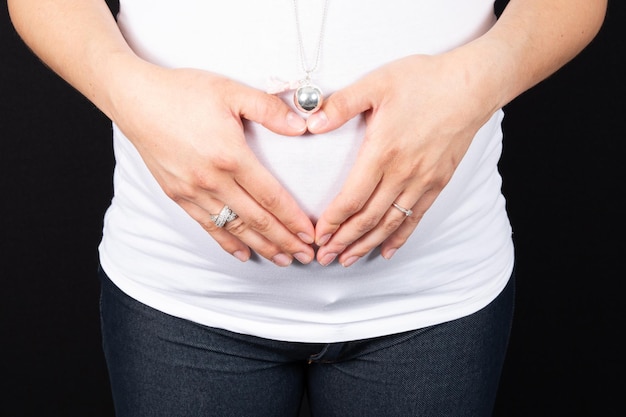 Vrouw die hartvorm op zwangere buik maakt met hun handen. concept van zwangerschap die een baby verwacht