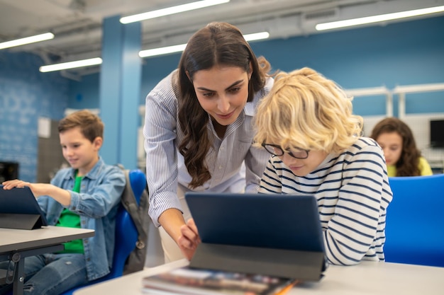 Vrouw die het tabletscherm van de jongen aan het bureau aanraakt