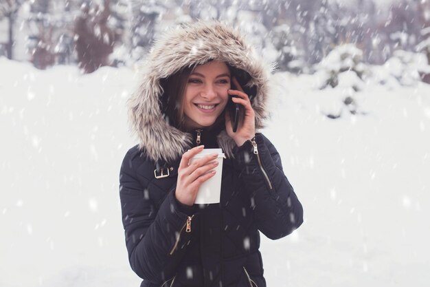 Vrouw die hete koffie of thee drinkt uit een mok onder sneeuwvlokken in de winter