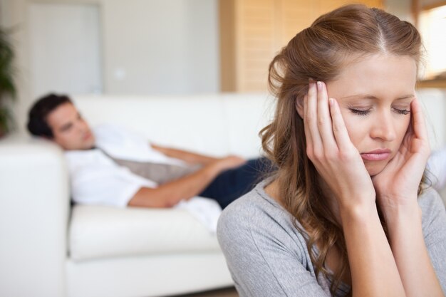 Vrouw die hoofdpijn met de mens op de bank achter haar ervaren