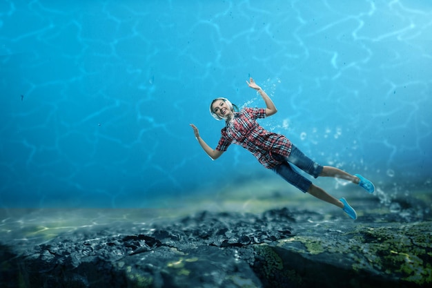 Vrouw die hoofdtelefoons draagt die onder water drijven. Gemengde media