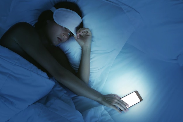 Vrouw die in bed ligt en 's nachts op smartphone kijkt