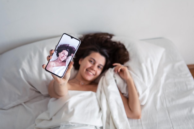 Vrouw die in bed ligt en selfie aan de telefoon neemt