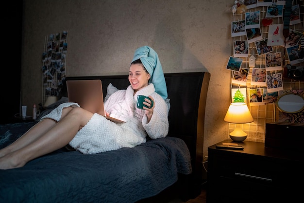 Vrouw die in bed ligt met een nat hoofd bedekt met een handdoek die op laptop werkt