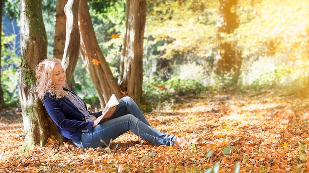 Vrouw die in de herfst een boek leest in het park
