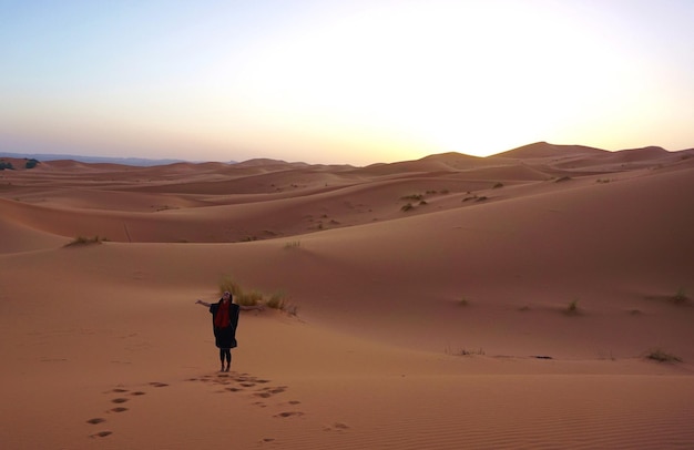 Vrouw die in de woestijn staat bij zonsondergang