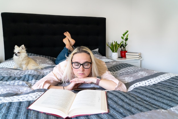 Vrouw die in een gezellig bed met haar hond ligt en een boek leest